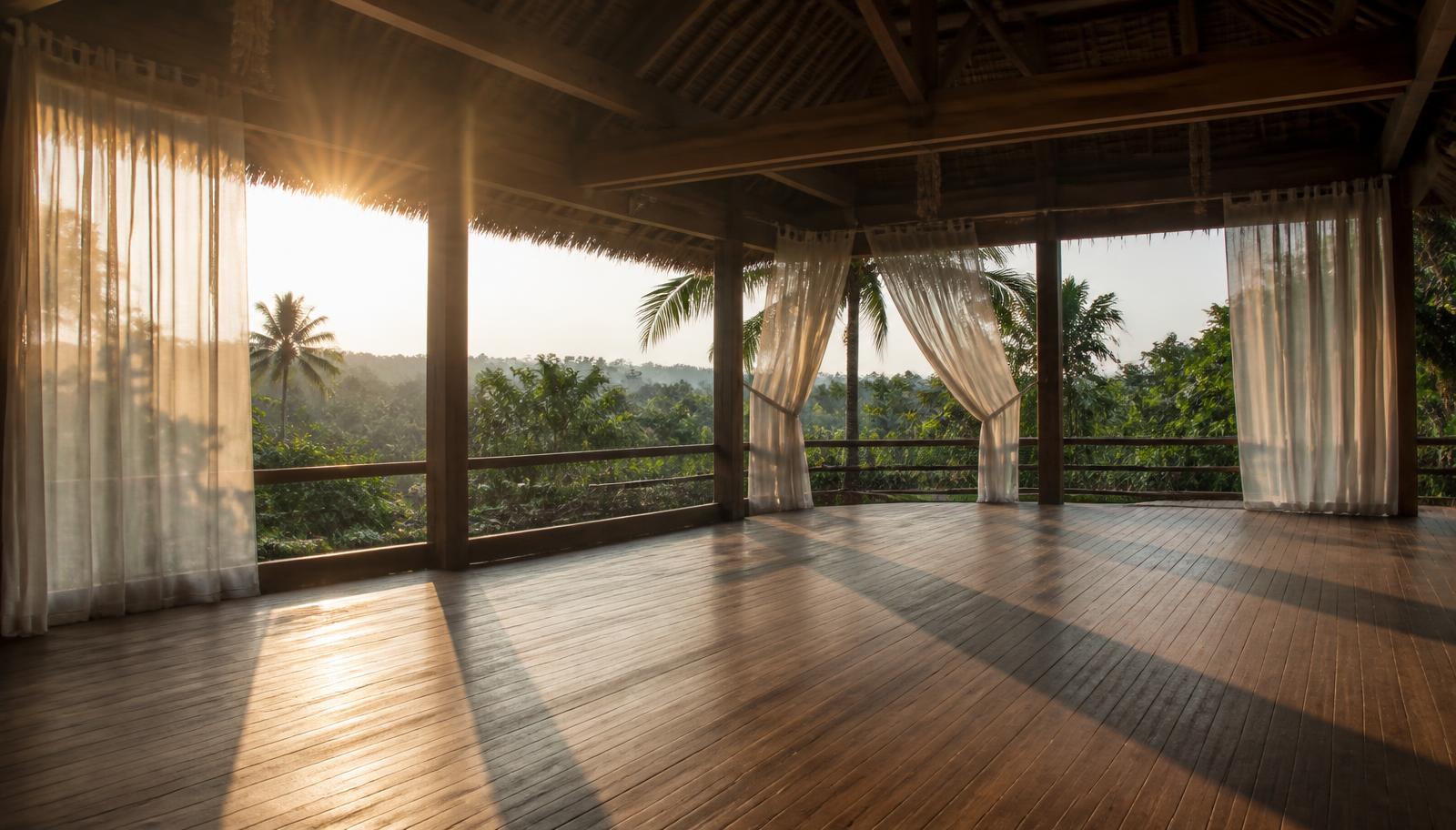 Open-air wooden studio deck at sunrise with curtains moving in the breeze