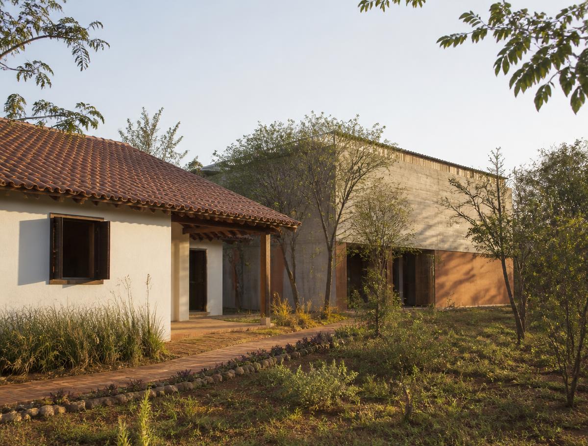 Casa simples de paredes claras ao lado de um galpão em transformação